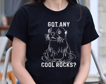 Puede incluir: Camiseta negra con un contorno blanco de una nutria y el texto "Got any cool rocks?"