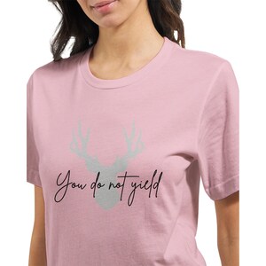 May include: A pink t-shirt with a gray deer silhouette and the text "You do not yield" in black.