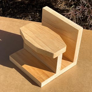 May include: A wooden shelf unit with two shelves. The top shelf is shaped like a hexagon and the bottom shelf is rectangular. The unit is made of light wood and has a natural finish.