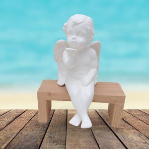 May include: A white ceramic angel figurine with wings, sitting on a wooden bench. The angel is blowing a kiss with its right hand.