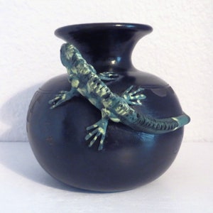 May include: Black ceramic vase featuring a green and black lizard design. The lizard is sculpted and painted in a realistic style.
