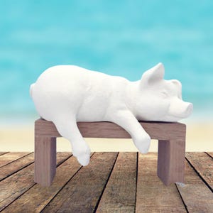May include: White ceramic pig figurine lying on a wooden bench. The pig has its eyes closed and is resting its head on the bench. The bench is made of light brown wood and has a simple design.