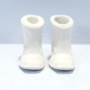 May include: A pair of white ceramic boots. The boots are plain and have a rounded toe.