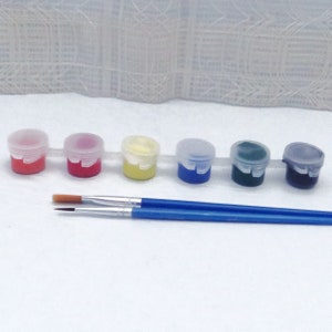 Op de afbeelding: Set van zes kleine verfpotjes met deksels, gevuld met rode, oranje, gele, blauwe, groene en zwarte verf. Twee kwasten zijn inbegrepen.