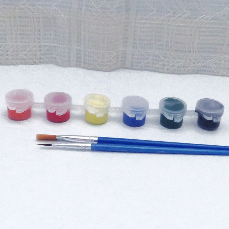 Op de afbeelding: Set van zes kleine verfpotjes met deksels, gevuld met rode, oranje, gele, blauwe, groene en zwarte verf. Twee kwasten zijn inbegrepen.
