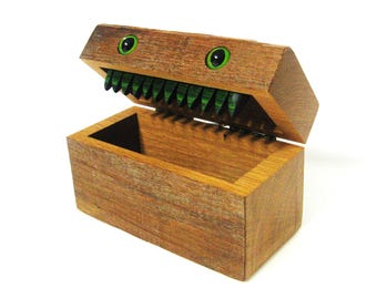 May include: A wooden box with a hinged lid, painted to look like a monster face with green eyes and teeth. The box is open, revealing the empty interior.
