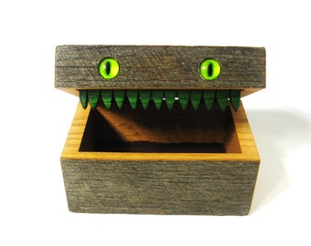 May include: A wooden box with a hinged lid, painted to look like a monster's open mouth with green teeth and glowing green eyes.