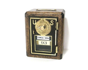 May include: A vintage wooden mailbox with a brass door and a circular dial with letters. The mailbox has a brass plaque that reads "CIRCA 1896" and a number "93".