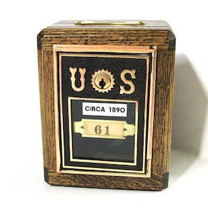 May include: Wooden antique mailbox with the letters "U.S" and a keyhole. The mailbox has a black front panel with gold trim and the text "CIRCA 1890" and the number "61". The wood has a natural grain.