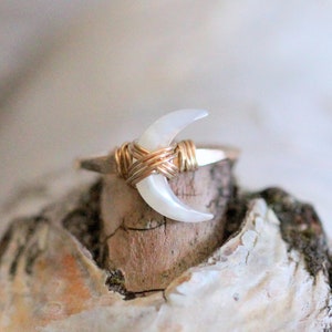 May include: A gold wire wrapped ring with a white crescent moon shaped stone.