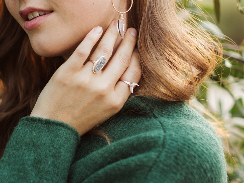K&ouml;nnte beinhalten: Eine Frau tr&auml;gt einen gr&uuml;nen Pullover mit zwei Ringen an ihren Fingern. Der Ring an ihrem Zeigefinger ist ein goldener Ring mit einem grauen Stein. Der Ring an ihrem kleinen Finger ist ein silberner Ring mit einem wei&szlig;en Stein.