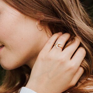 K&ouml;nnte beinhalten: Ein goldener Ring mit einem wei&szlig;en Halbmond-Design. Der Ring wird am Zeigefinger einer Hand getragen.