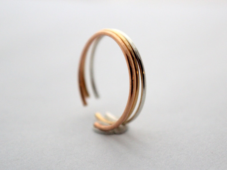 May include: A triple band ring with three different colored metal bands. The bands are silver, gold, and rose gold.