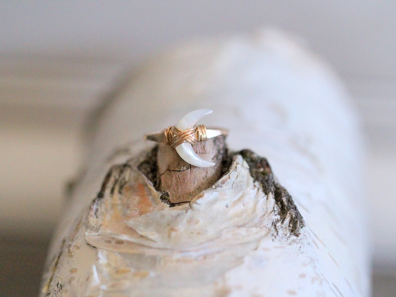 May include: A gold wire wrapped ring with a white crescent moon shaped stone.