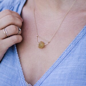 May include: A gold necklace with a delicate chain and a small, irregular-shaped, yellow gemstone pendant.