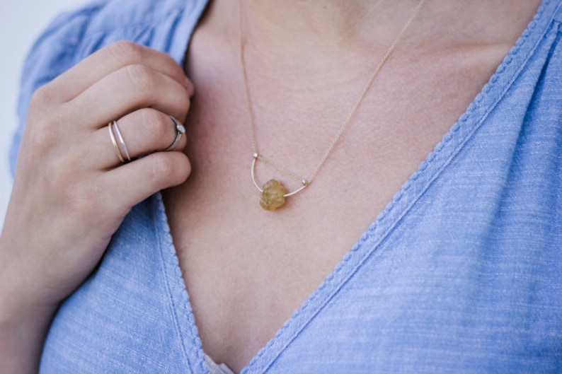 May include: A gold necklace with a delicate chain and a small, irregular-shaped, yellow gemstone pendant.