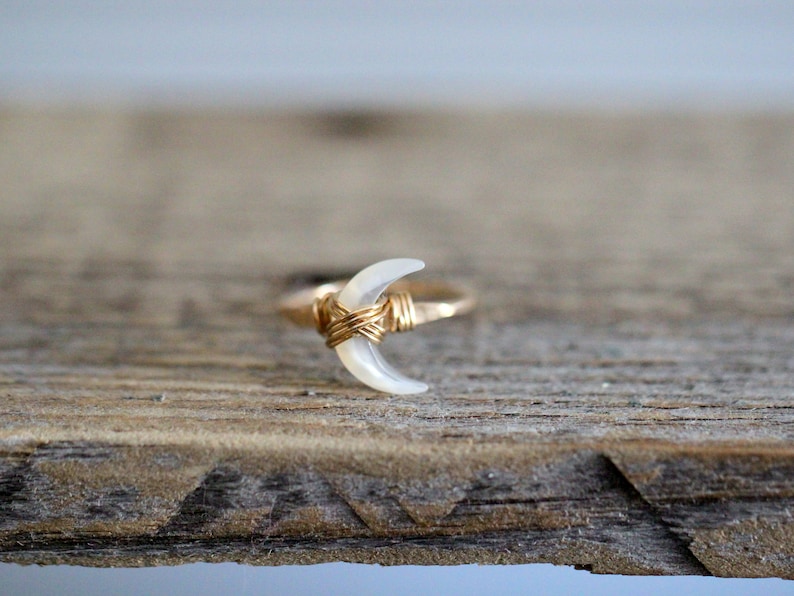 K&ouml;nnte beinhalten: Ein goldener Drahtring mit einer wei&szlig;en, halbmondf&ouml;rmigen Muschel.