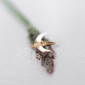 K&ouml;nnte beinhalten: Ein goldener Ring mit einem wei&szlig;en, sichelf&ouml;rmigen Stein. Der Ring ist mit Golddraht umwickelt.