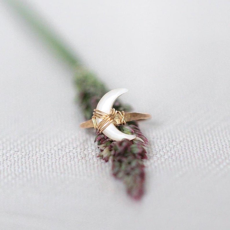 K&ouml;nnte beinhalten: Ein goldener Ring mit einem wei&szlig;en, sichelf&ouml;rmigen Stein. Der Ring ist mit Golddraht umwickelt.