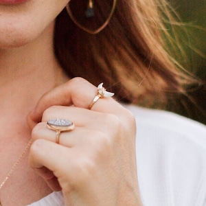 K&ouml;nnte beinhalten: Eine Frauenhand tr&auml;gt drei goldene Ringe. Die Ringe sind ein Halbmond mit einem wei&szlig;en Stein, ein d&uuml;nner Band und ein gro&szlig;er ovaler Ring mit einem grauen Stein.