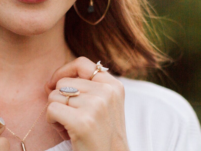 K&ouml;nnte beinhalten: Eine Frauenhand tr&auml;gt drei goldene Ringe. Die Ringe sind ein Halbmond mit einem wei&szlig;en Stein, ein d&uuml;nner Band und ein gro&szlig;er ovaler Ring mit einem grauen Stein.