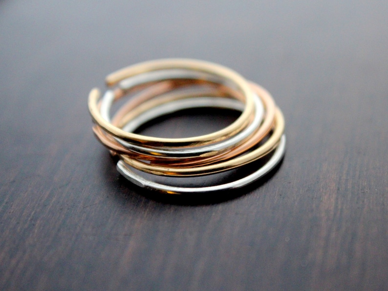 May include: A set of three thin, stacked rings in silver, gold, and rose gold.