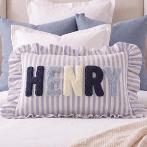 A decorative pillow with the name "HENRY" printed on it, surrounded by various other pillows and bedding items.