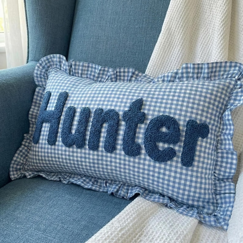 A blue and white gingham pillow with the name "Hunter" embossed on it, placed on a blue armchair.