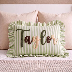 A decorative pillow with the name "Taylor" embroidered on it, placed on a bed with other pillows.