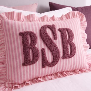A pink and white striped pillow with the letters "BSB" embroidered on it.
