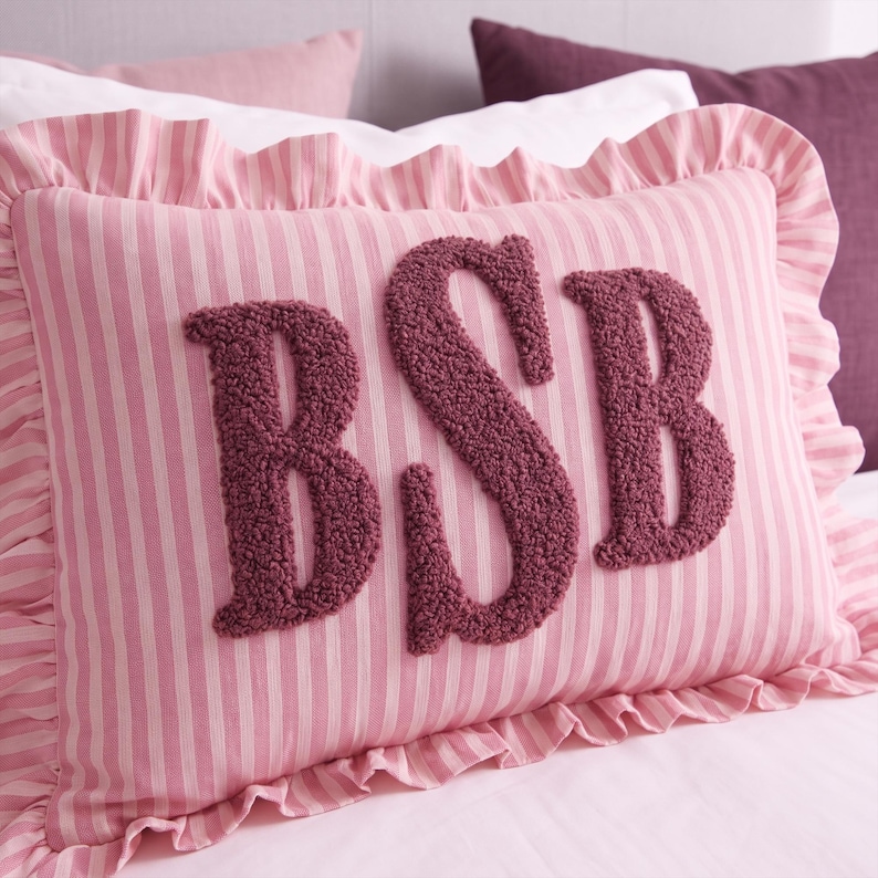 A pink and white striped pillow with the letters "BSB" embroidered on it.