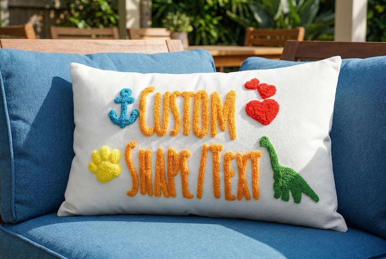 A white pillow with colorful embroidered text and shapes, including a blue anchor, a red heart, a yellow paw print, and a green dinosaur, sits on a blue couch.