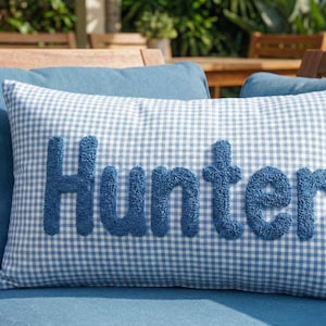 A blue and white checkered pillow with the word "Hunter" embroidered on it, placed on a blue couch.