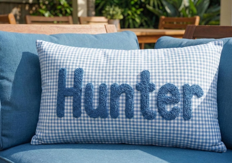 A blue and white checkered pillow with the word "Hunter" embroidered on it, placed on a blue couch.