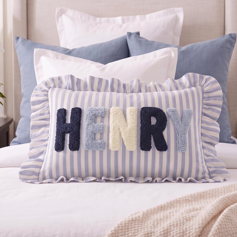 A decorative pillow with the name "HENRY" printed on it, surrounded by various other pillows and bedding items.