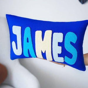 A person is holding a blue pillow with the name "James" embroidered on it.