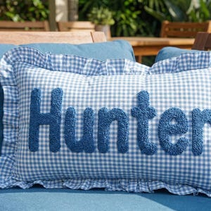 A blue and white gingham pillow with the name "Hunter" embroidered on it, placed on a blue couch.