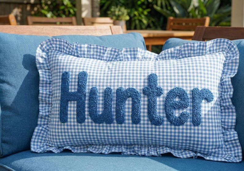 A blue and white gingham pillow with the name "Hunter" embroidered on it, placed on a blue couch.