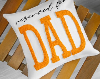 Puede incluir: Almohada blanca con el texto "reservado para PAPÁ" en letras naranjas hinchadas.