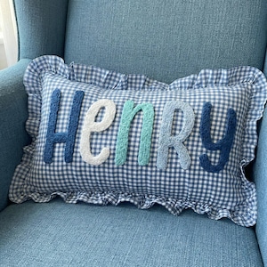 A blue and white checkered pillow with the name "HENRY" embroidered on it, sitting on a blue chair.