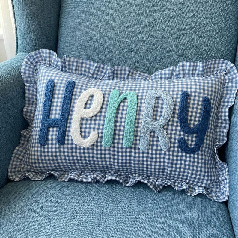 A blue and white checkered pillow with the name "HENRY" embroidered on it, sitting on a blue chair.