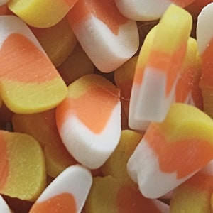 May include: A close-up of a pile of candy corn. The candy corn is yellow, orange, and white.