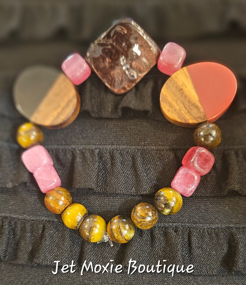 May include: A bracelet with tiger's eye beads, pink and red gemstone beads, and wooden beads. The bracelet has a silver clasp.