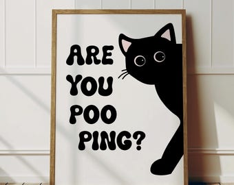 Op de afbeelding: Een ingelijste kunstprint met een zwarte kat die van rechts tevoorschijn komt. De tekst "ARE YOU POO PING?" staat in vette, afgeronde letters op een witte achtergrond. De lijst is lichtbruin.