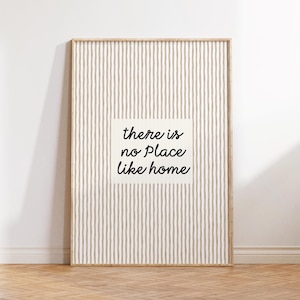 Può includere: Opera d'arte da parete incorniciata con sfondo a righe beige e bianche. Un quadrato bianco al centro presenta il testo "there is no place like home" in nero. La cornice è in legno chiaro.