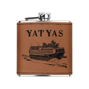May include: A brown leather-wrapped flask with a silver top and a black engraved image of an amphibious assault vehicle. The text "YAT YAS" is engraved above the image.