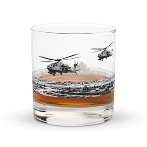 May include: A clear glass tumbler filled with amber liquid, featuring a detailed black and white etched illustration of two military attack helicopters flying over a desert landscape with mountains and small buildings in the background.