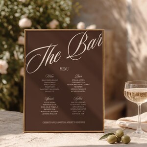 Puede incluir: Un letrero de menú de bar rectangular con fondo marrón oscuro y marco dorado. El texto dice The Bar, Menu, Wine, Beer, Spirits, Softies y enumera varios nombres de bebidas. En la parte inferior, dice Cheers to love, laughter & a night to remember.