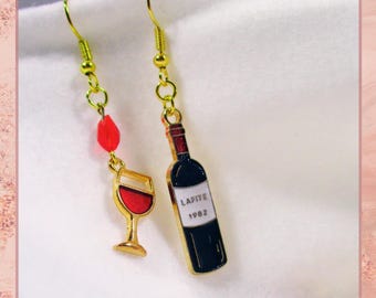 May include: Gold earrings with red glass beads and charms of a wine bottle and a wine glass. The bottle charm has the text "Lafite 1982" on the label.