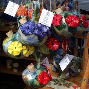 May include: A collection of colorful ceramic bottle stoppers with floral designs. The stoppers are hand-painted with various flowers, including red, blue, and yellow. Each stopper has a cork insert for sealing bottles.